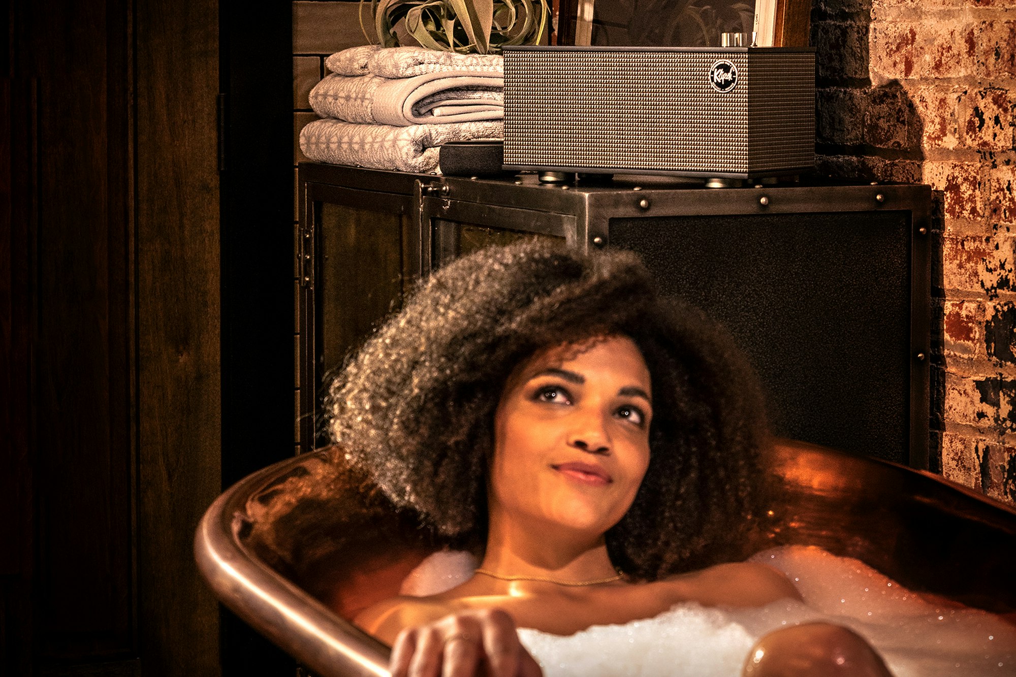 Estéreo de sobremesa One II de Klipsch junto a una mujer en una bañera